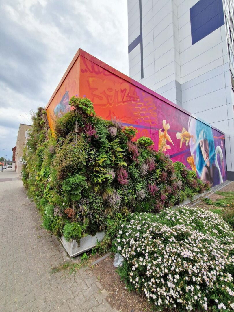 Heizhaus mit Graffitimotiv einer Frau mit blauen Haaren und einem Goldfischglas über dem Kopf. Daneben ist ein Motiv eines Flamingos.